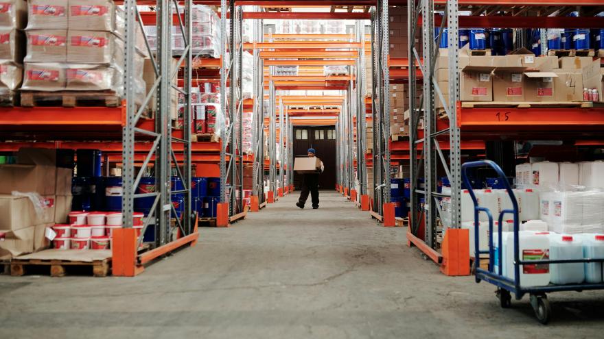 Man_Standing_in_an_Aisle_of_a_Warehouse_Carrying_a_Box