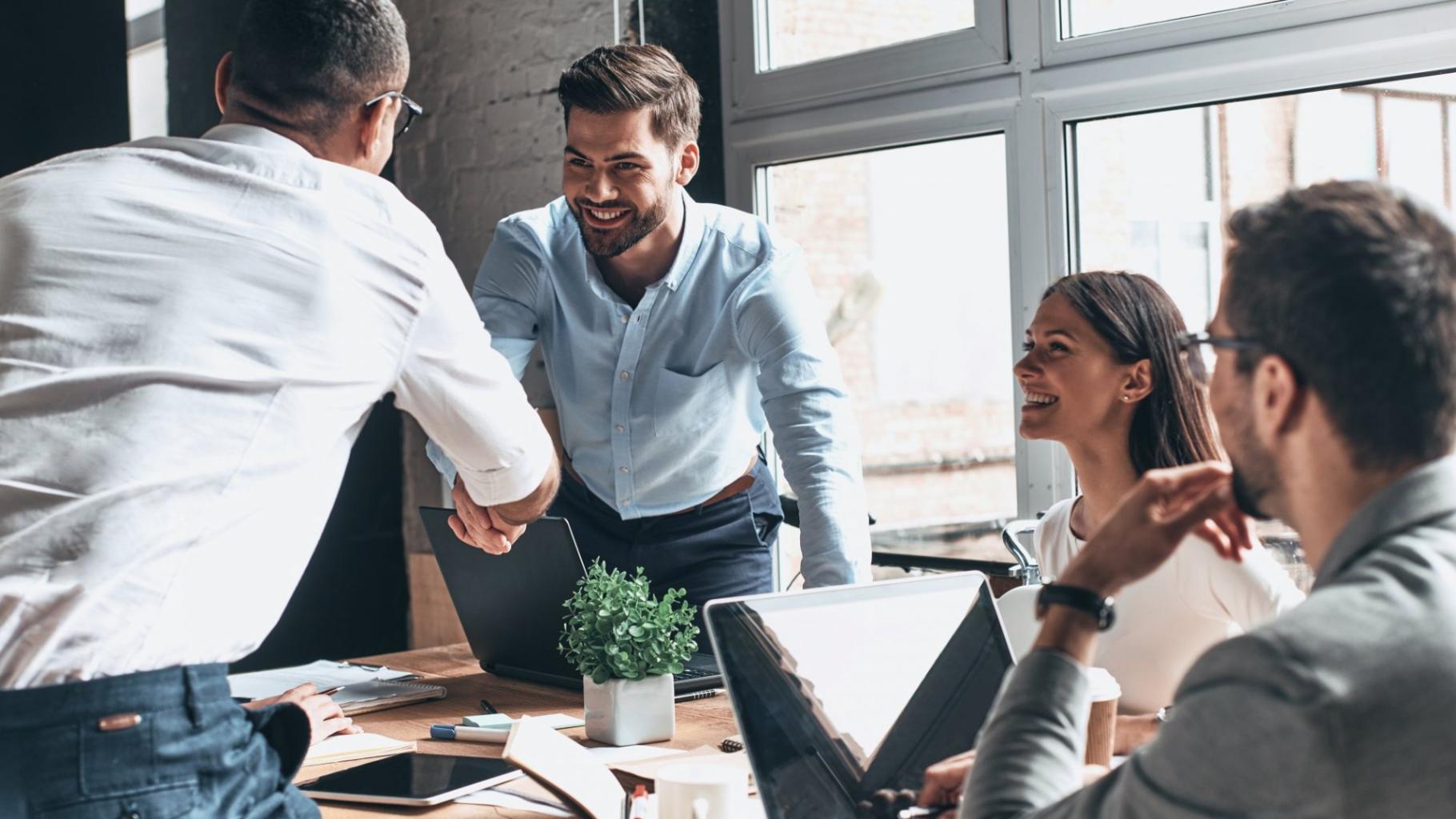 person_shaking_hands_with_another_person_while_coworkers_look_on