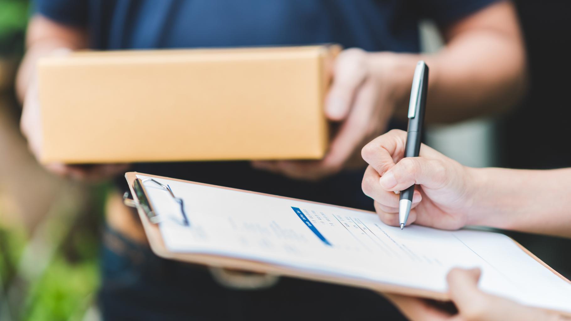 Hand-putting-signature-in-clipboard-to-receive-package-from-delivery-man